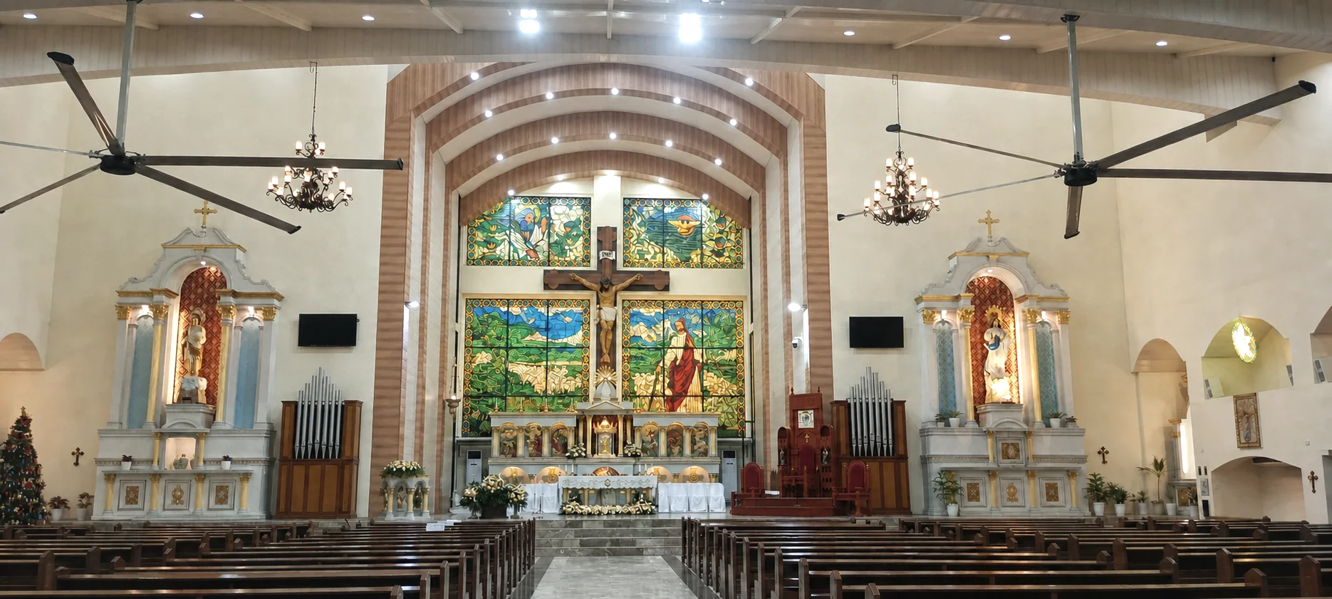 Wide sanctuary view with altar, stained glass, chandeliers, and pews