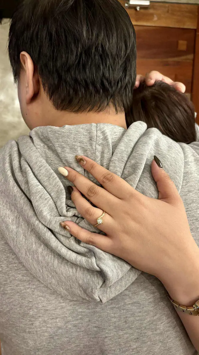 Maila's polished nails and engagement ring resting on Carlo's shoulder